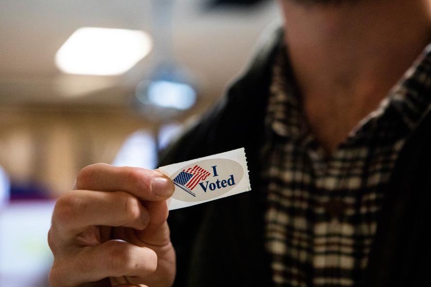 A person holding up a sticker that reads "I voted" with an American flag