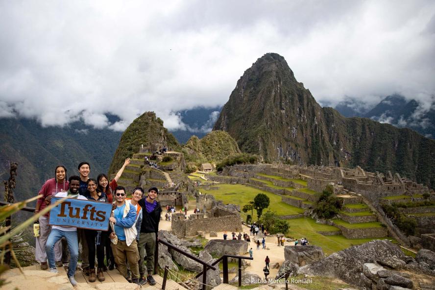 Tufts University students holding a Tufts University banner outside ruins in Peru