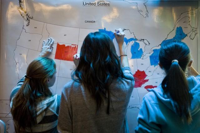 three people using markers to color in a map of the United States of America