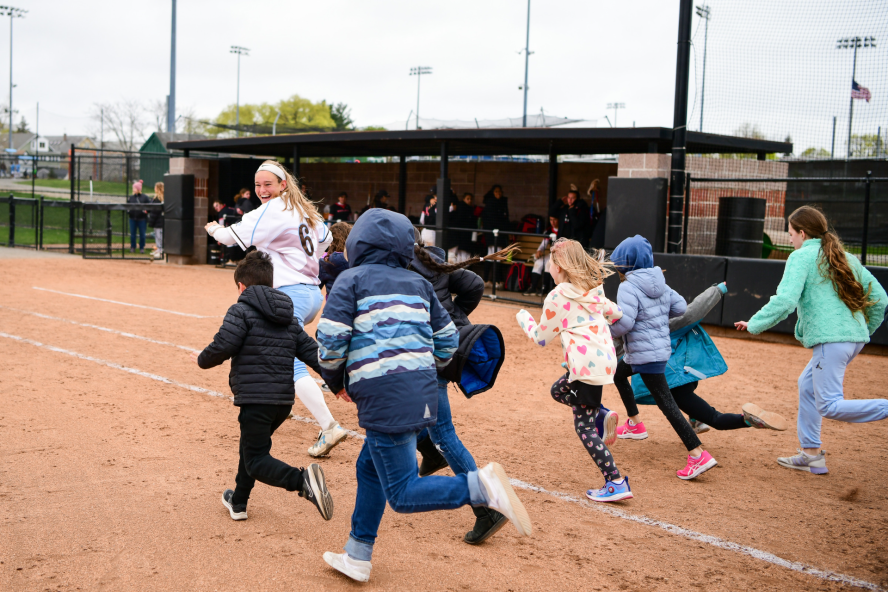 softball team members running with children on a softball game