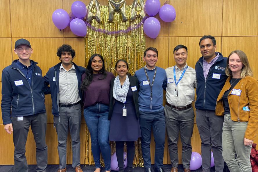 Medical School Students pose in front of a wall with purple and gold balloons that spell out "AMA"