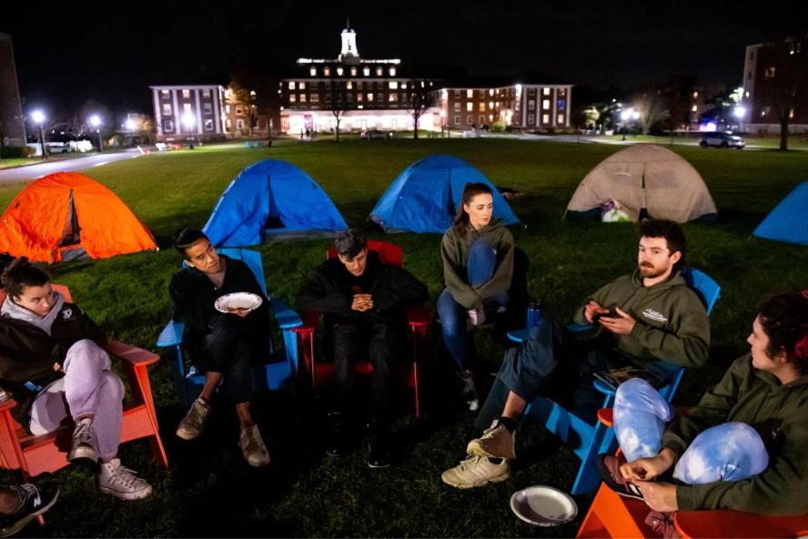 Students sit around the residential quad at night in lawn chairs with tents during the Sleepout