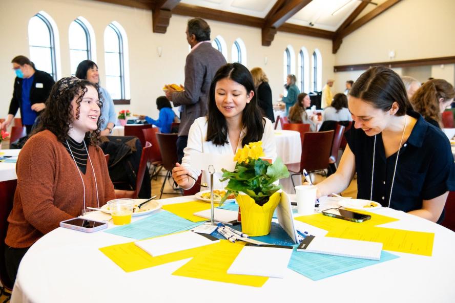 Symposium attendees sit around a table with colored papers in Breed Hall at Tufts