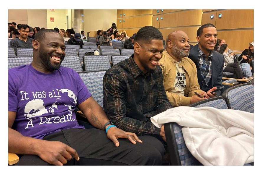 4 men sitting the row of an auditorium laughing with each other