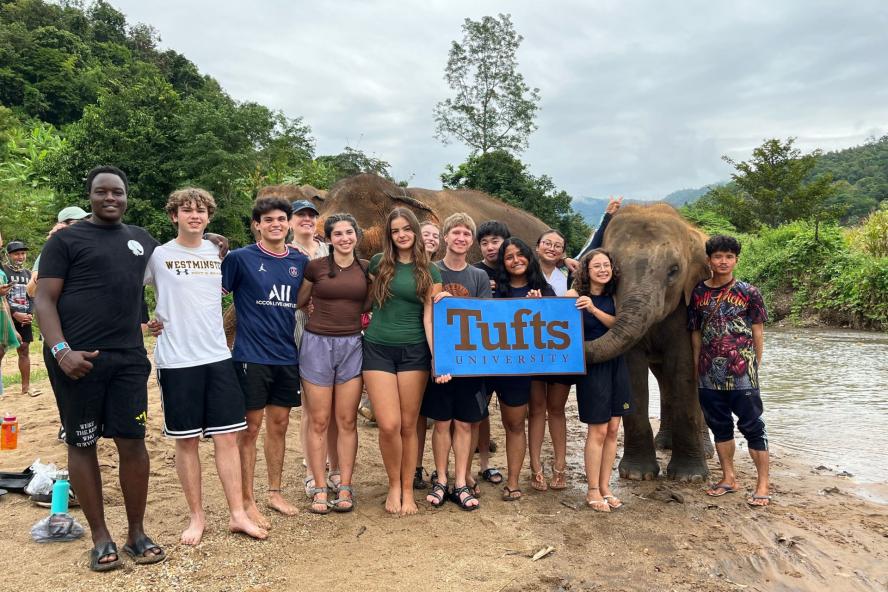 Civic Semester students in Thailand pose with an elephant and a Tufts flag