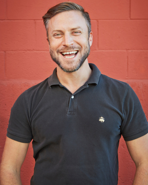 Noah Wilson Rich smiles in front of a red brick background