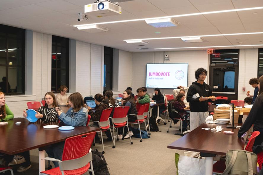 Students sit at tables with JumboVote logo and name on a screen