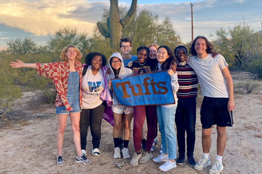 Civic Semester students pose with Tufts flag in front of a large cactus in the Southwest