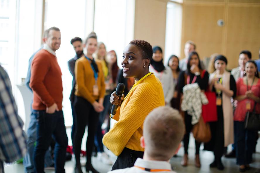 A woman speaks into a microphone while others look on at a symposium