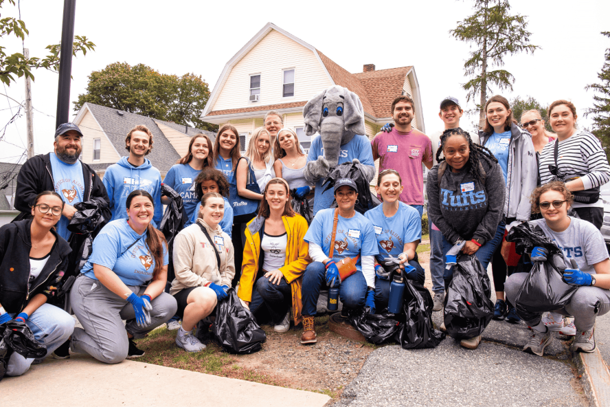 Group of people wearing Tufts gear smiling with the Jumbo mascot. 