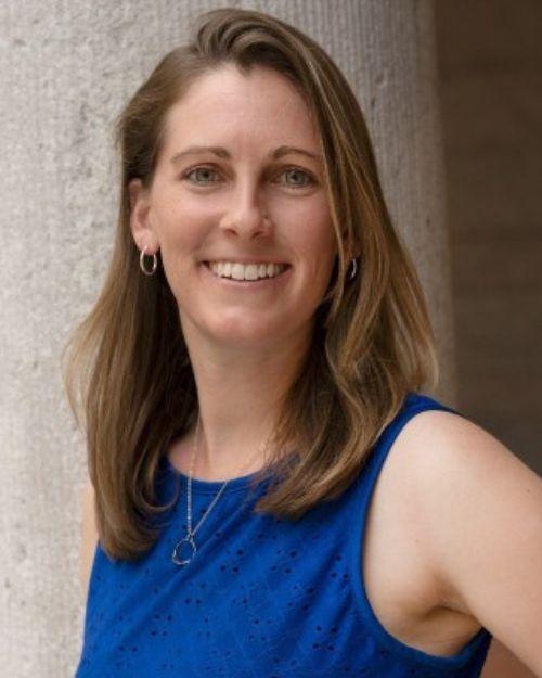 Woman with brown hair in a blue blouse smiling.