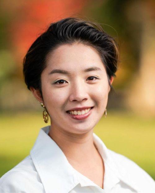 Young woman in a white shirt looks straight ahead and smiles. 