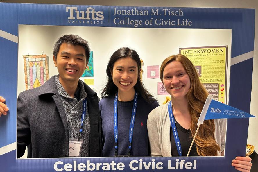 Three Tufts alumni pose with a frame and a Tisch College flag
