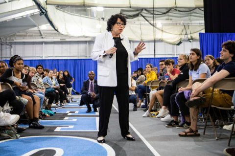 Sonia Sotomayor speaking into a microphone while standing in the aisle between large crowds of seated people