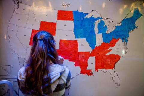 A young woman looks at a national map divided between red and blue states