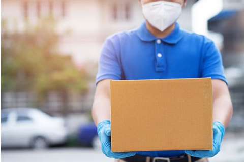 person wearing a blue polo, medical mask, and medical gloves carrying a brown box