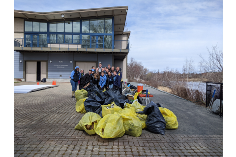 Tufts students pose in front of the Boathouse along the river with garbage bags