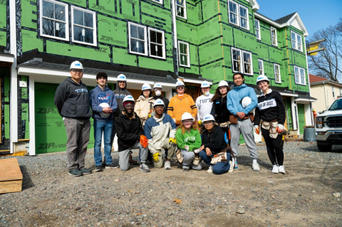 A group of students and staff pose in front of a house under construction. A group of students stayed at Tufts and spent time in nearby communities during their Jumbo Spring Break