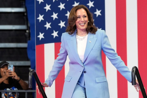 Kamala Harris walks up a few stairs, with a large U.S. flag in the background. A political scientist explains the surprising role that gender plays in American politics